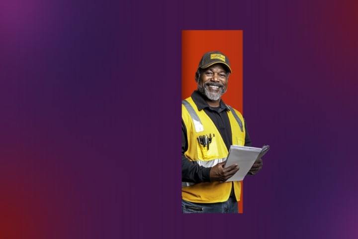 A man in safety vest and 'American Freight' cap smiling with a clipboard in hand.