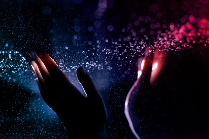 Two hands surrounded by glowing light particles on a gradient blue-to-red background. 