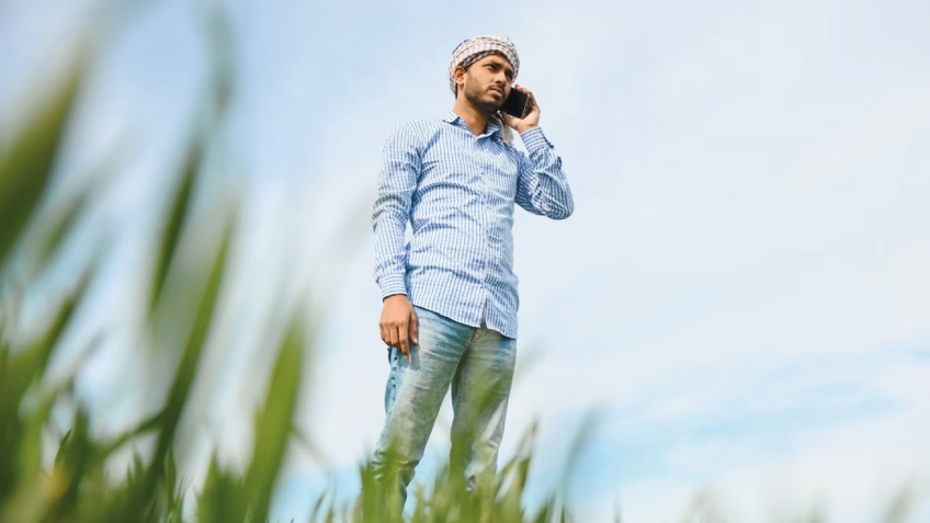 A person talks on a smartphone while standing in a green field.