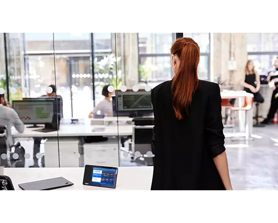 Femme aux cheveux rouges et blazer noir marchant loin du bureau où ThinkSmart View Zoom est assis.