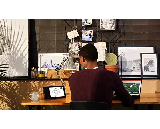 ThinkSmart View Zoom assis sur un bureau brun en bois avec des photos et un homme travaillant à ThinkSmart View Zoom tout en travaillant sur le portable ThinkPad.