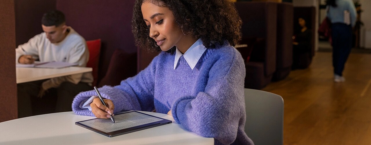 Student at a library desk with Lenovo Smart Paper E-Ink reader laid flat, making notes on screen with Lenovo Smart Pen