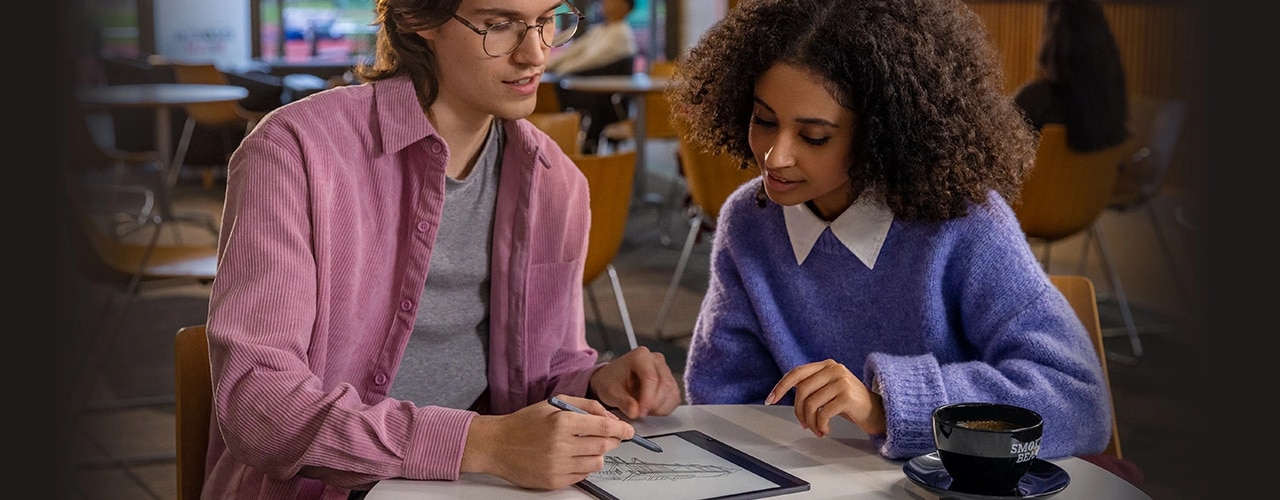 Two students in a cafe with Lenovo Smart Paper E-Ink reader laid flat, with one student making notes on screen with Lenovo Smart Pen