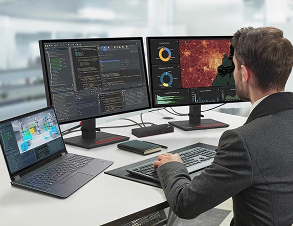 Ein Spieleentwickler betrachtet einen Code auf zwei großen Monitoren, links daneben steht ein geöffnetes Lenovo ThinkPad P16 Gen 2 (16