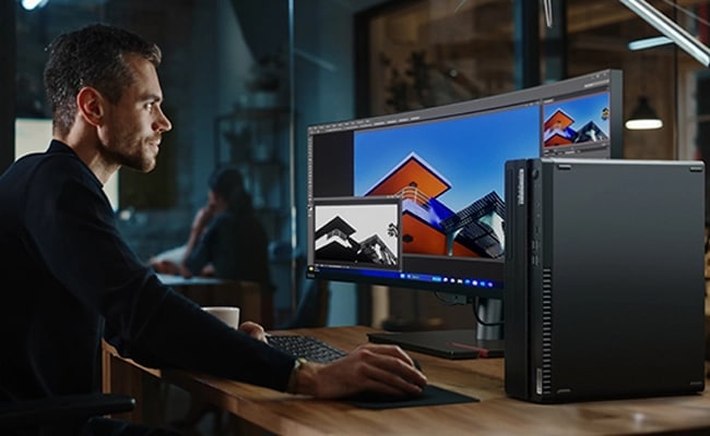 用家坐在書桌前，使用前景擺放的 Lenovo ThinkCentre M90s Gen 5 小型機型個人電腦工作，旁邊有 Lenovo ThinkVision 曲面屏幕、鍵盤及滑鼠。